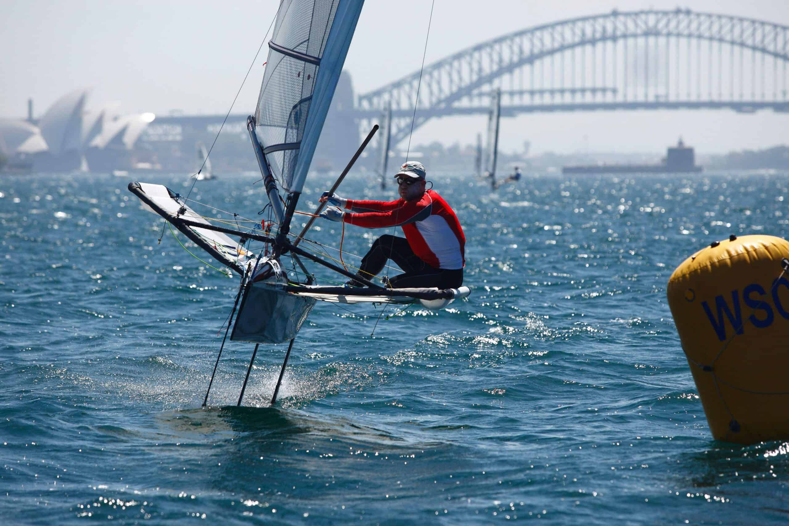 Sailor in red jacket racing a sailboat near Sydney Harbour Bridge.
